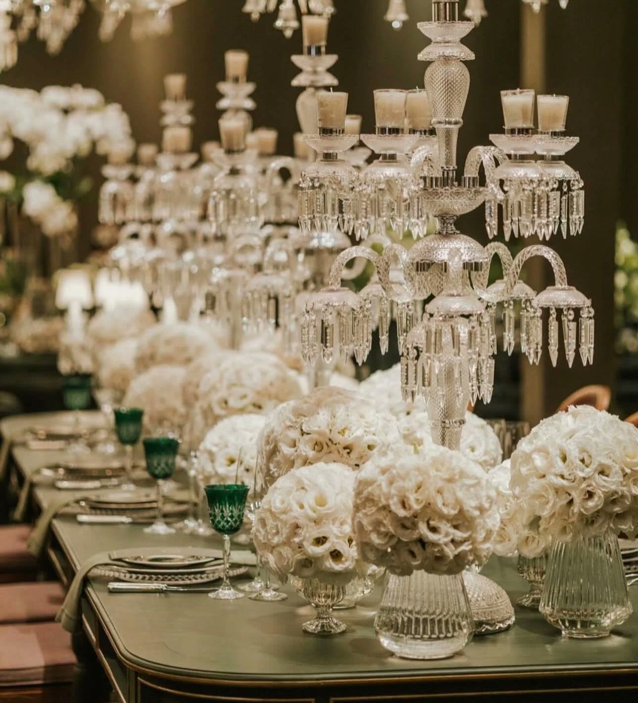 Mesa posta com candelabros de cristal, arranjos de flores brancas e taças verdes