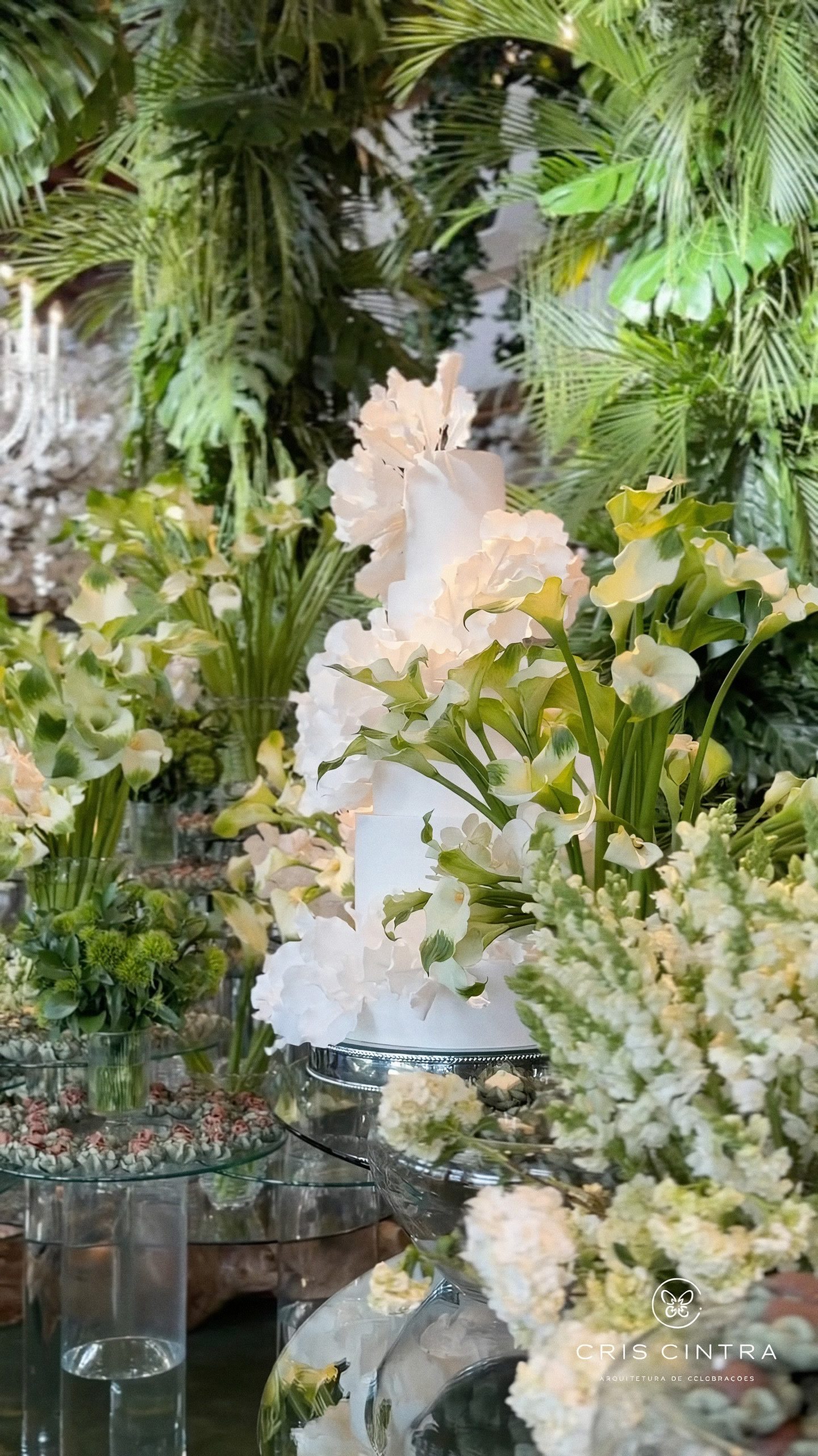 Bolo branco cercado por flores e folhagens verdes